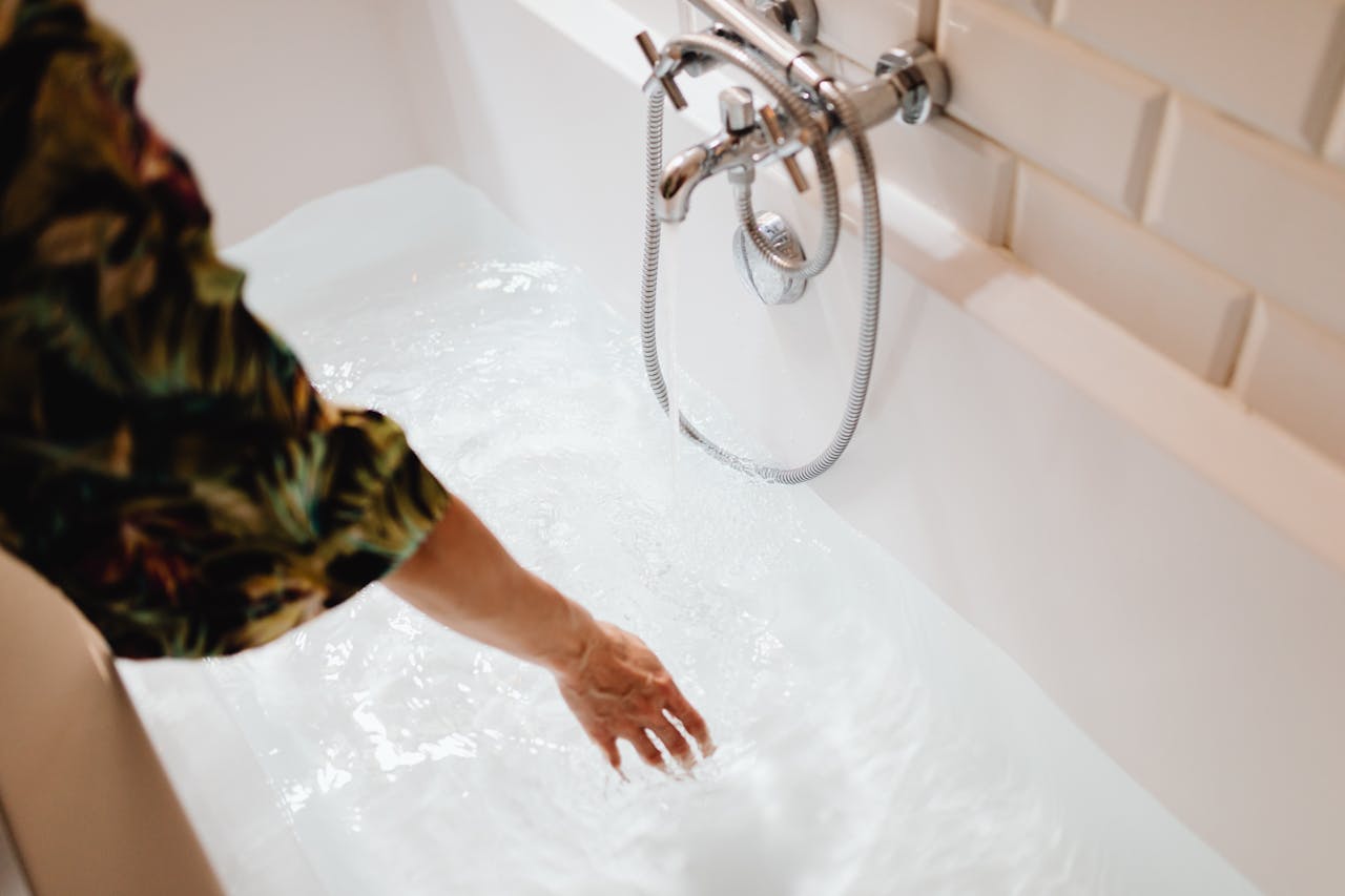 A close-up image of a hand touching water in a bathtub, focusing on the serene moment.